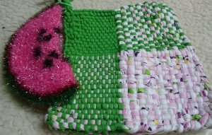Ein Paar grüne mit rosa-weissen Garn gewebteTopflappen, dazu einen schönen Wassermelonenschwamm in rosa