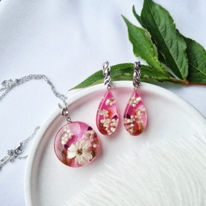 Schöne Ohrringe und Anhänger mit Blumen auf rosa Hintergrund.