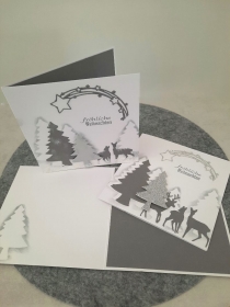 Schöne Weihnachtskarte mit Tannenbäume und einer Rentierfamilie alles in weis und Silber gehalten