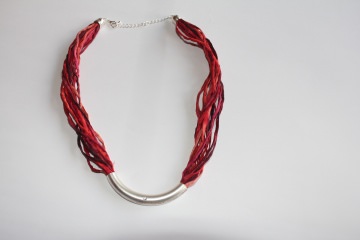 Halskette aus Seidenschnüre in verschiedenen Rottönen mit einem silberfarbenen Schmuckstück mit einem kleinen Glitzerstein